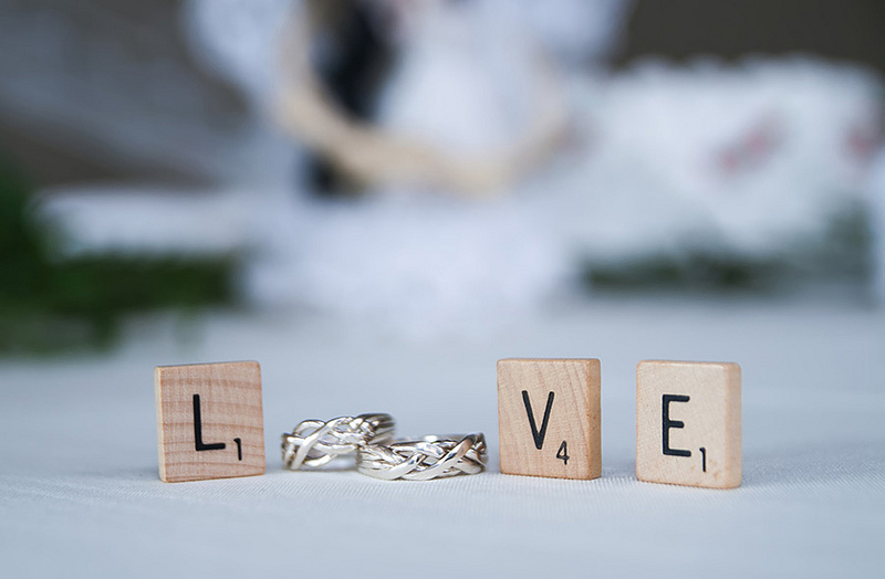 Scrabble pieces spelling Love with L, V, and E, wedding rings are used for the O