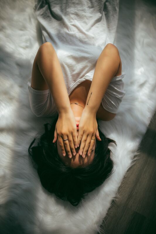 Sad Caucasian Woman laying on white fur, hands covering her eyes
