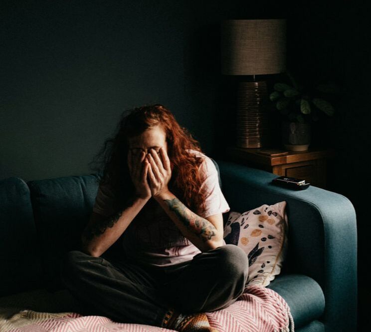 Emotional woman with red hair sitting on couch with her head in her hands