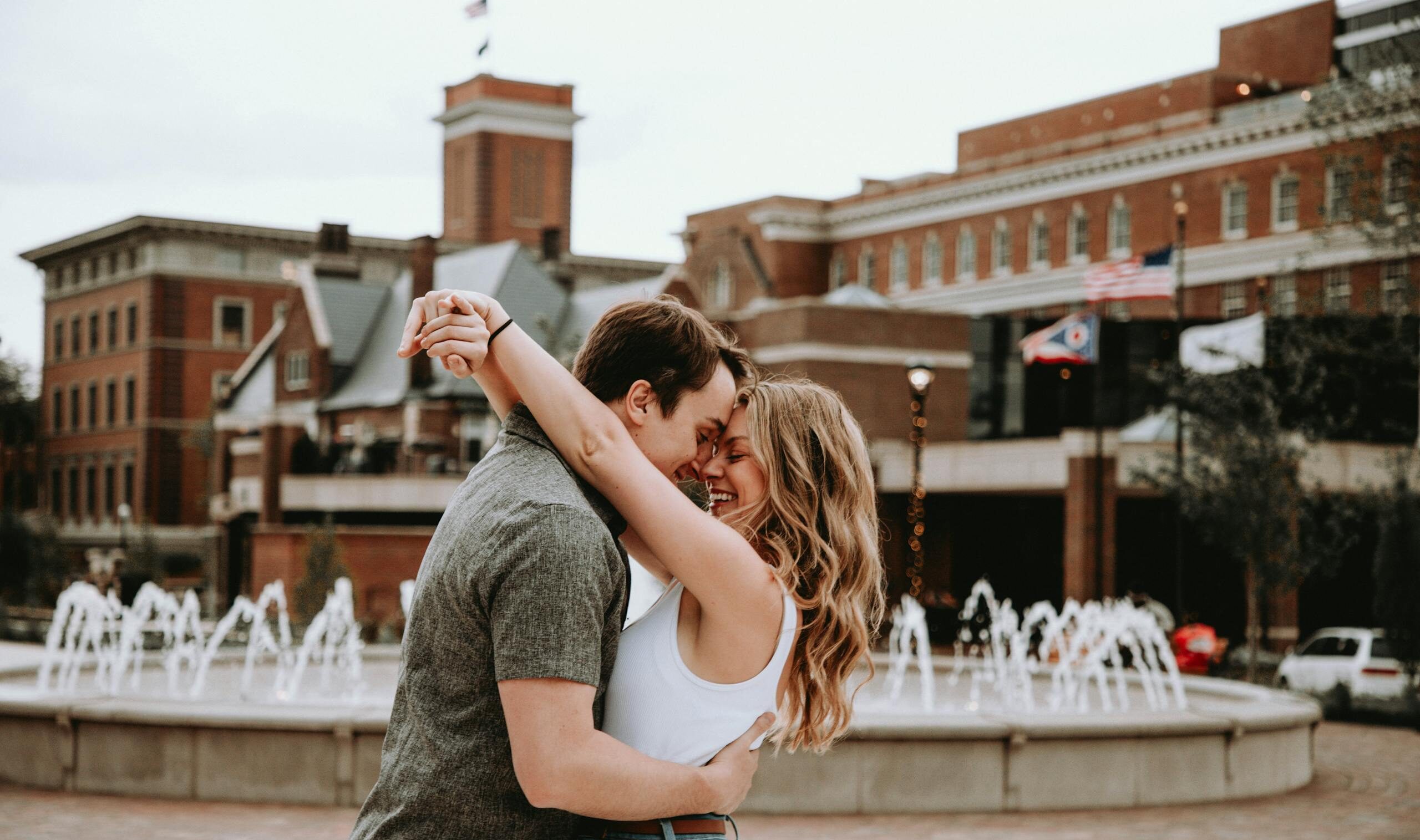 Young couple embracing lovingly near a fountain in Cincinnati's urban setting.